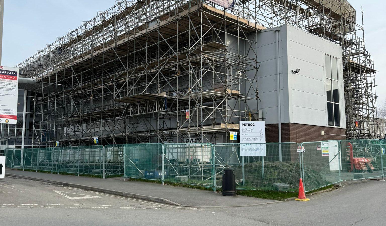 Large building with commercial scaffolding in North Devon, surrounded by green fencing and signs.