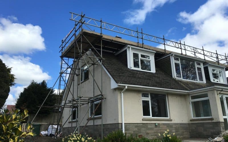 Two-storey house with domestic scaffolding on the roof, set against a blue sky with white clouds.